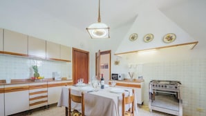 Een keuken met een eettafel voor vier personen, houten kastjes, een fornuis en een hangende lamp.