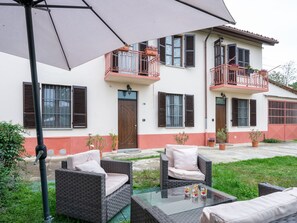 Een gebouw met twee verdiepingen, een balkon, een terras met rieten meubels en potplanten.
