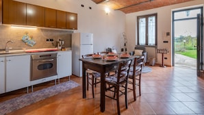 A kitchen with wooden cabinets, a white refrigerator, and a dining area with a table and chairs. - Casa dei Nonni by Interhome (Calliano)