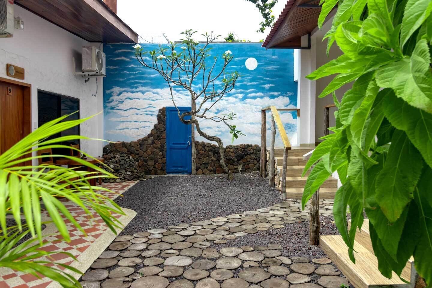 A courtyard with a tree, a blue door, and a stone pathway.