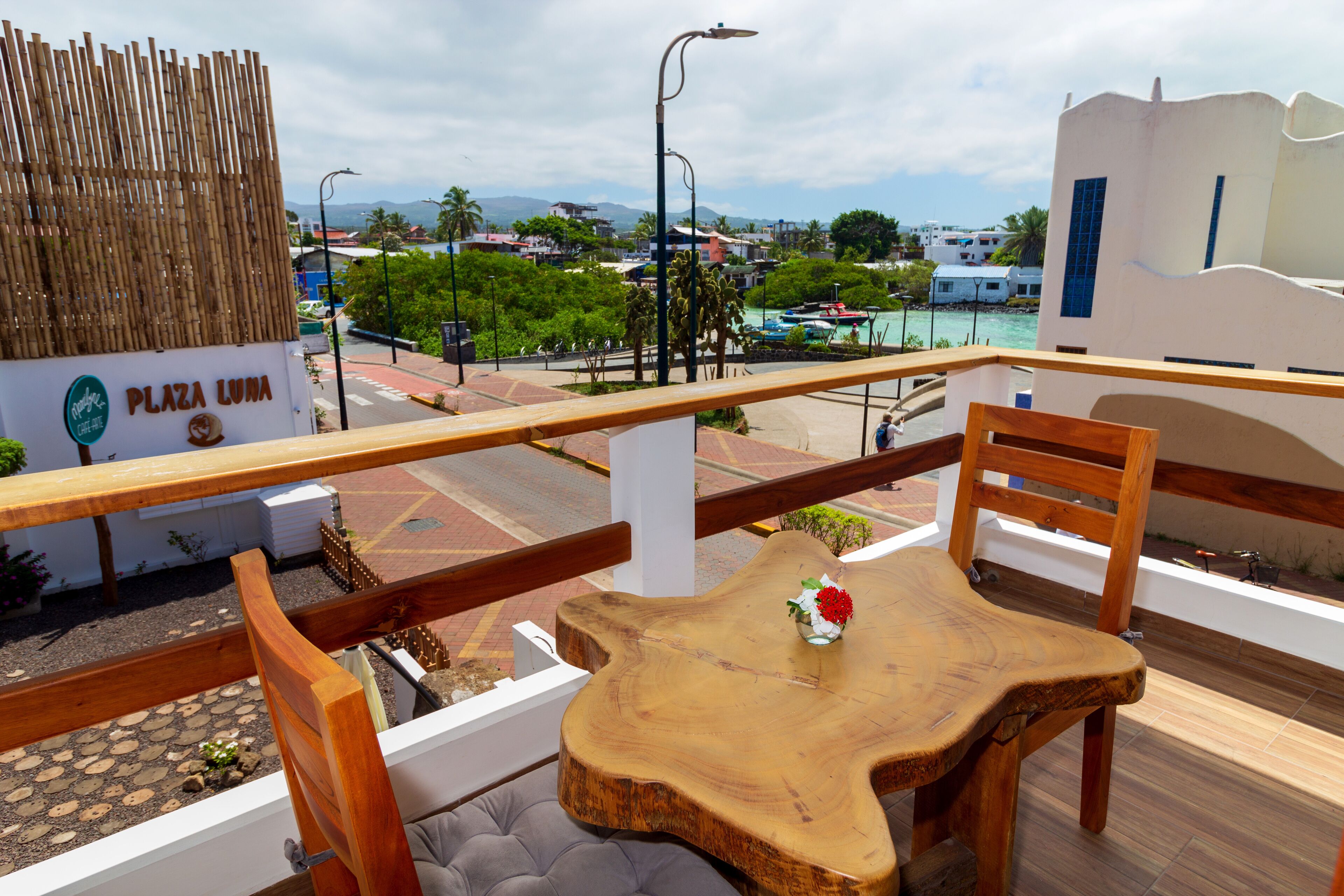 Una mesa y sillas de madera en un balcón exterior con vista a una playa y edificios al fondo.