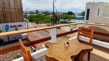 Una mesa y sillas de madera en un balcón exterior con vista a una playa y edificios al fondo.