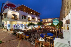 A restaurant with outdoor seating, a sign for 'Marlyn's Cafe-Arte', and a 'Roland' store across the street.