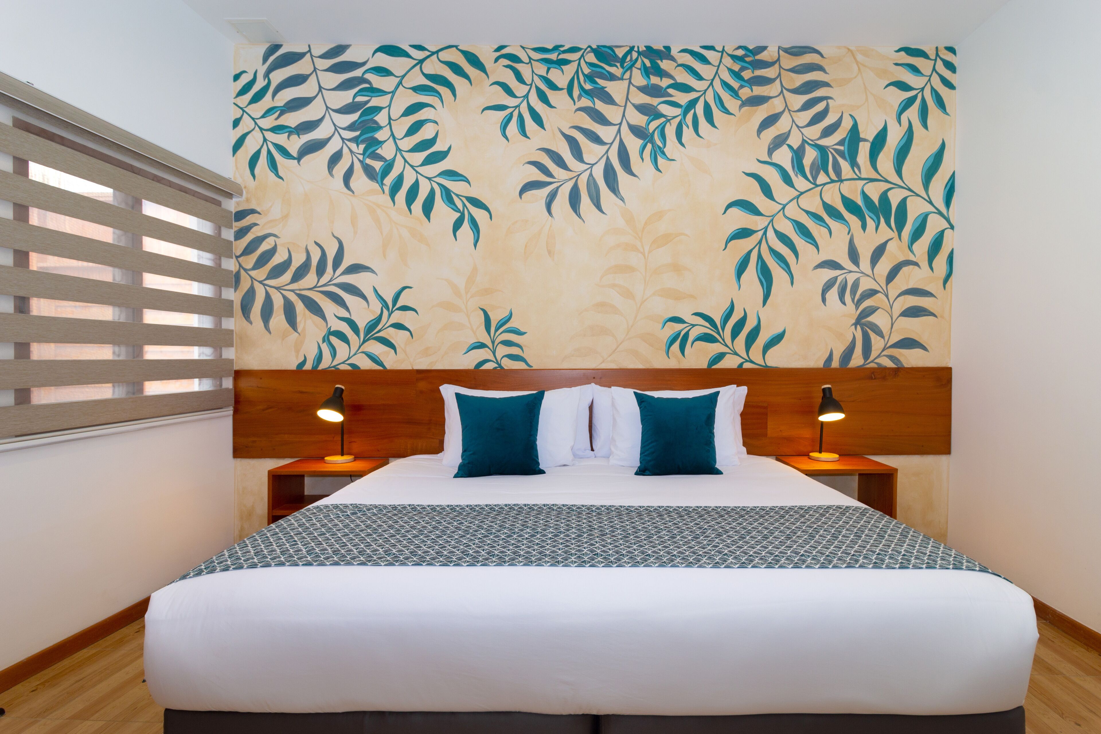 A neatly made bed with a patterned bedspread, two bedside lamps, and a wall with a leaf pattern.