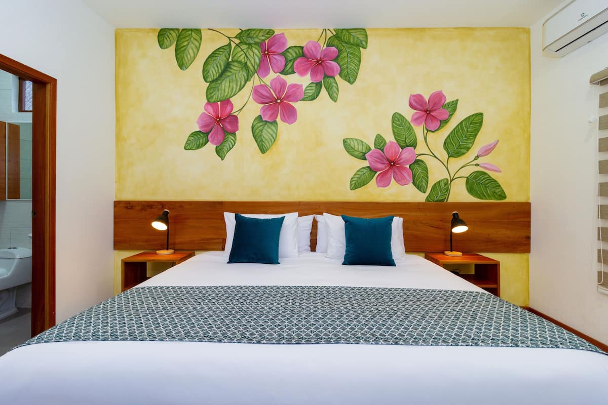 Une chambre d’hôtel avec un lit, deux tables de chevet, une lampe fixée au mur et une fresque murale à motifs floraux.