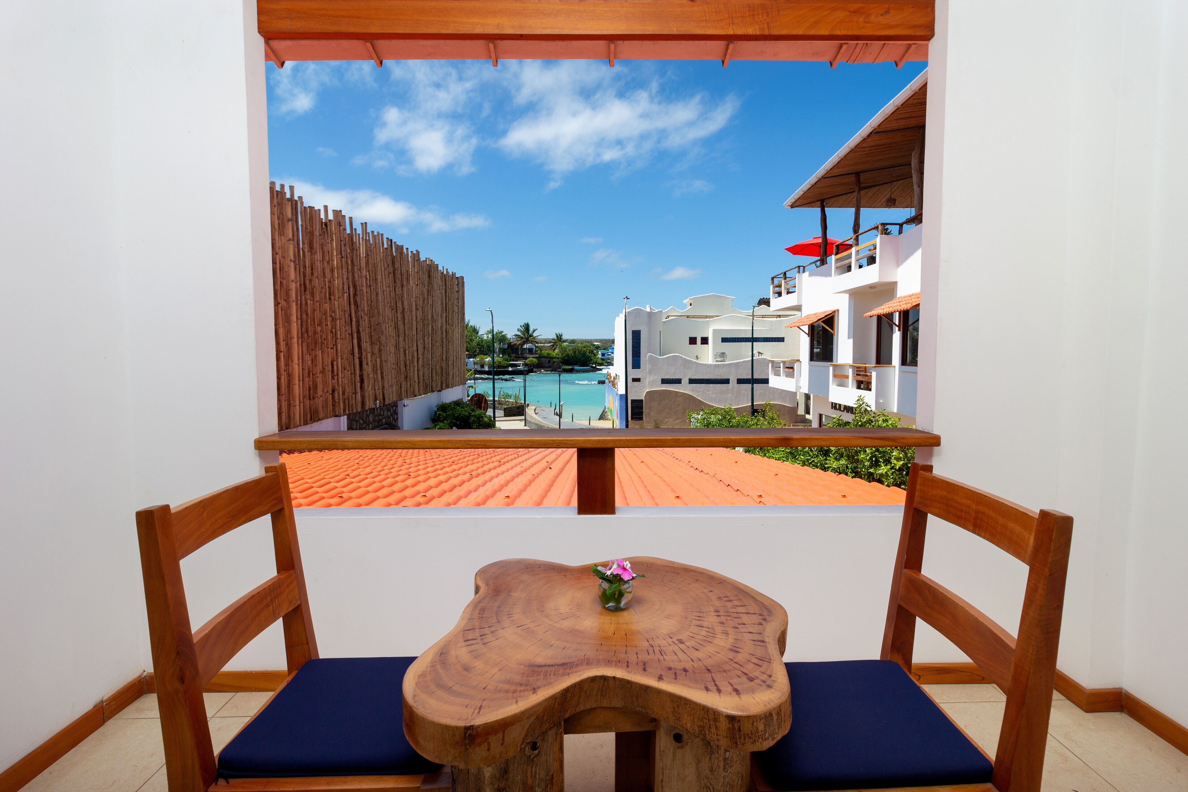 Una panca in legno con un tavolo e cuscini, con vista su una piscina e degli edifici.