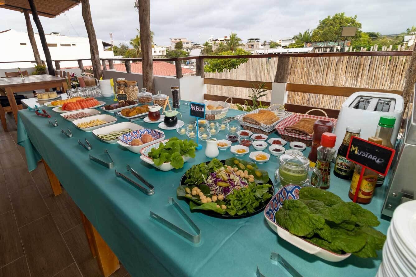 A buffet table with various food items and condiments, set outdoors with a view of buildings in the background.