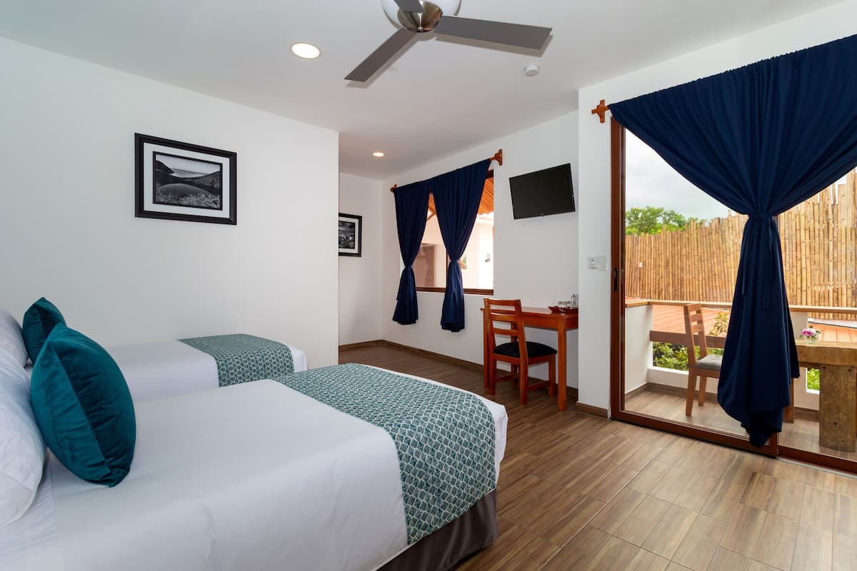 Une chambre d’hôtel avec deux lits, un bureau, une chaise, un ventilateur de plafond et une vue sur l’extérieur.