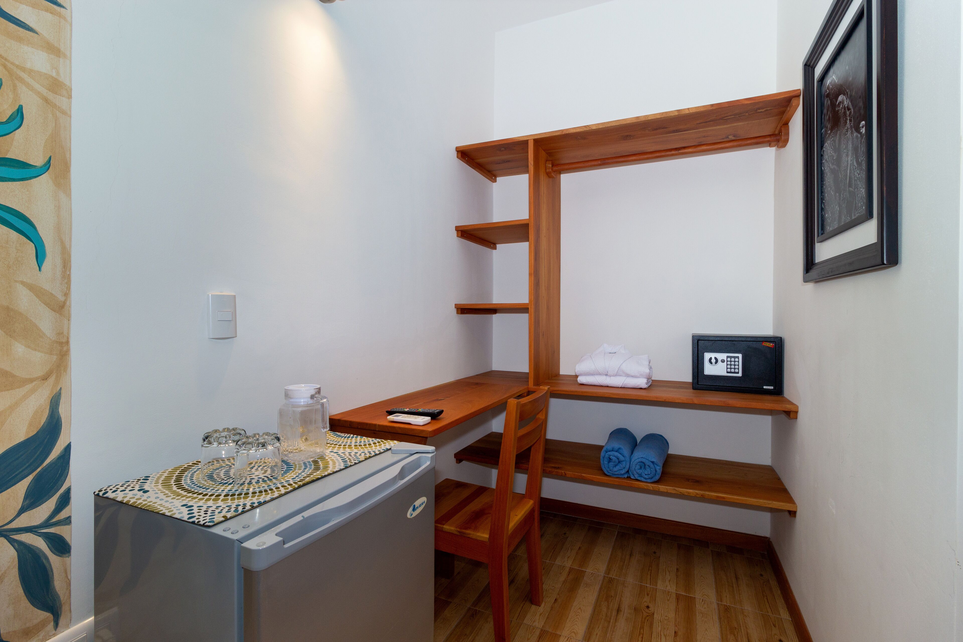 A compact room with a wooden desk, a small refrigerator, a microwave, and a shelf with towels.
