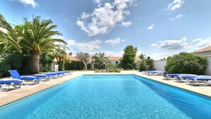 A rectangular swimming pool with clear blue water, surrounded by lounge chairs and palm trees. - Le Moulin de la Filasse by Interhome (Ile d'Oléron)