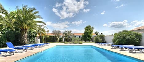 A rectangular swimming pool with clear blue water, surrounded by lounge chairs and palm trees.
