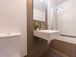 Ein Badezimmer mit Toilette, Waschbecken inklusive Spiegel und Duschbereich.