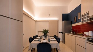 A modern dining room with a long table set for six, kitchen cabinets, and a red backsplash.