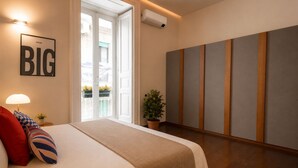 A hotel room with a bed, a wall-mounted air conditioner, a potted plant, and a large framed sign.