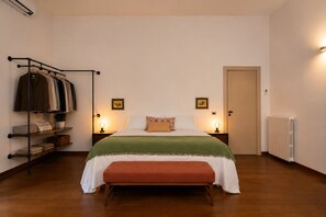 A bedroom with a bed, bedside tables with lamps, a bench, a radiator, and a clothing rack.