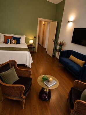 A hotel room with a bed, two sofas, a small table with a book, and a TV on the wall.