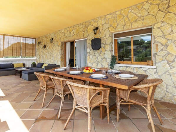 An outdoor dining area with a stone wall, wicker chairs, and a table set for four.