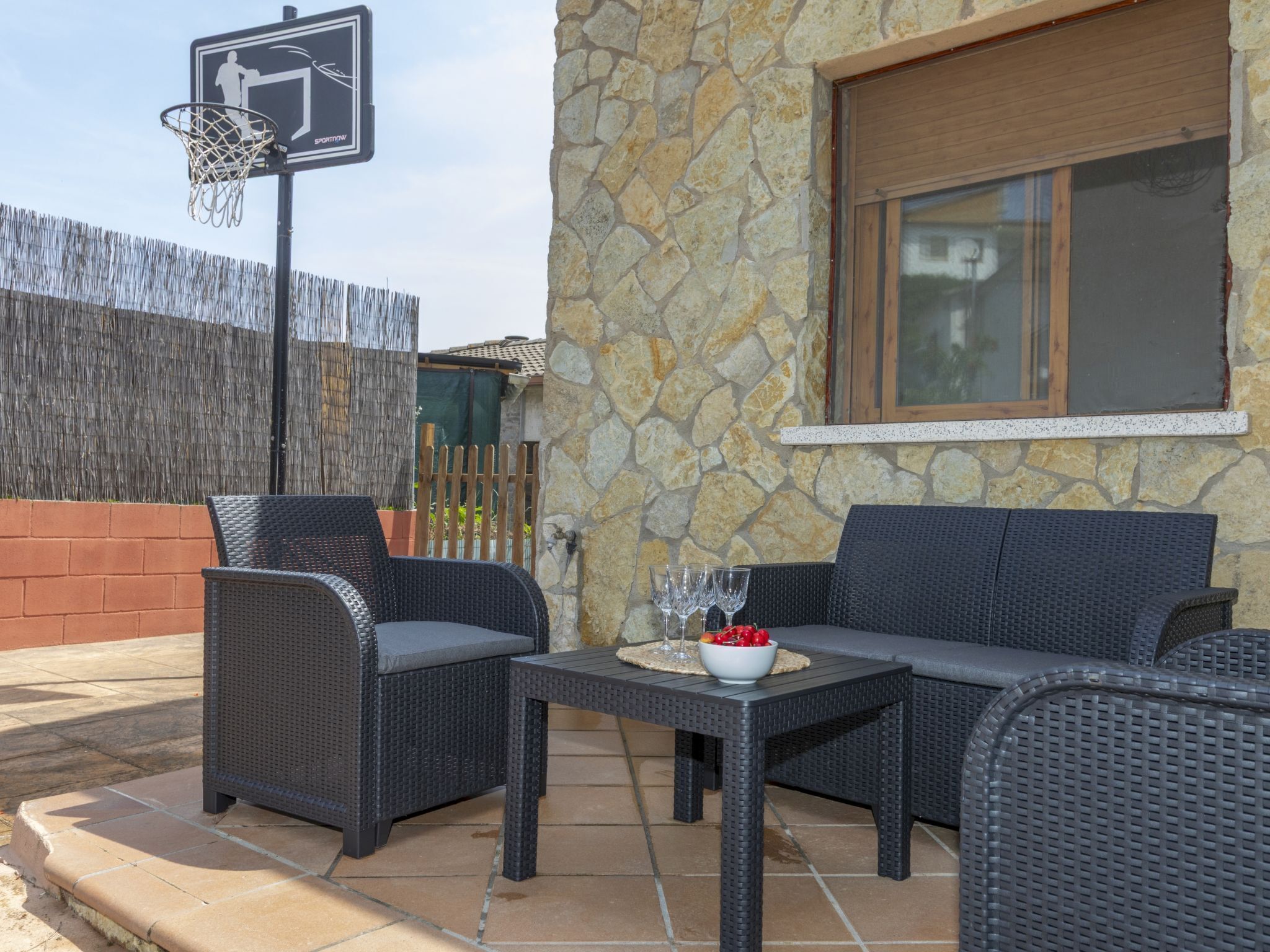 An outdoor seating area with wicker furniture, a stone wall, and a basketball hoop.