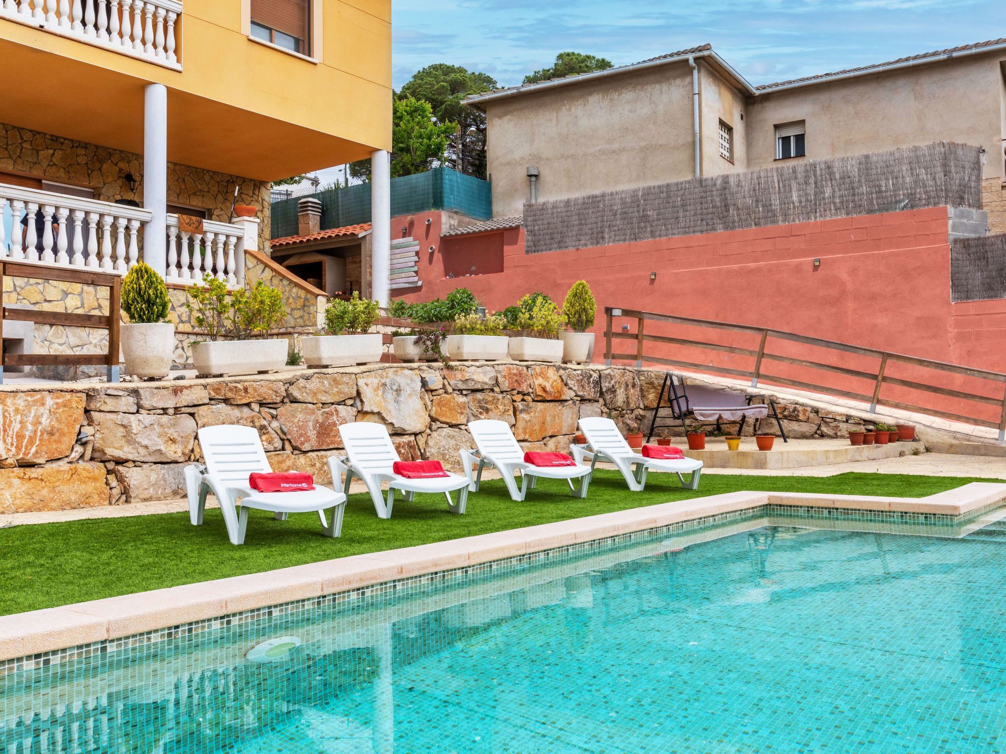 A pool area with white lounge chairs and a stone wall.