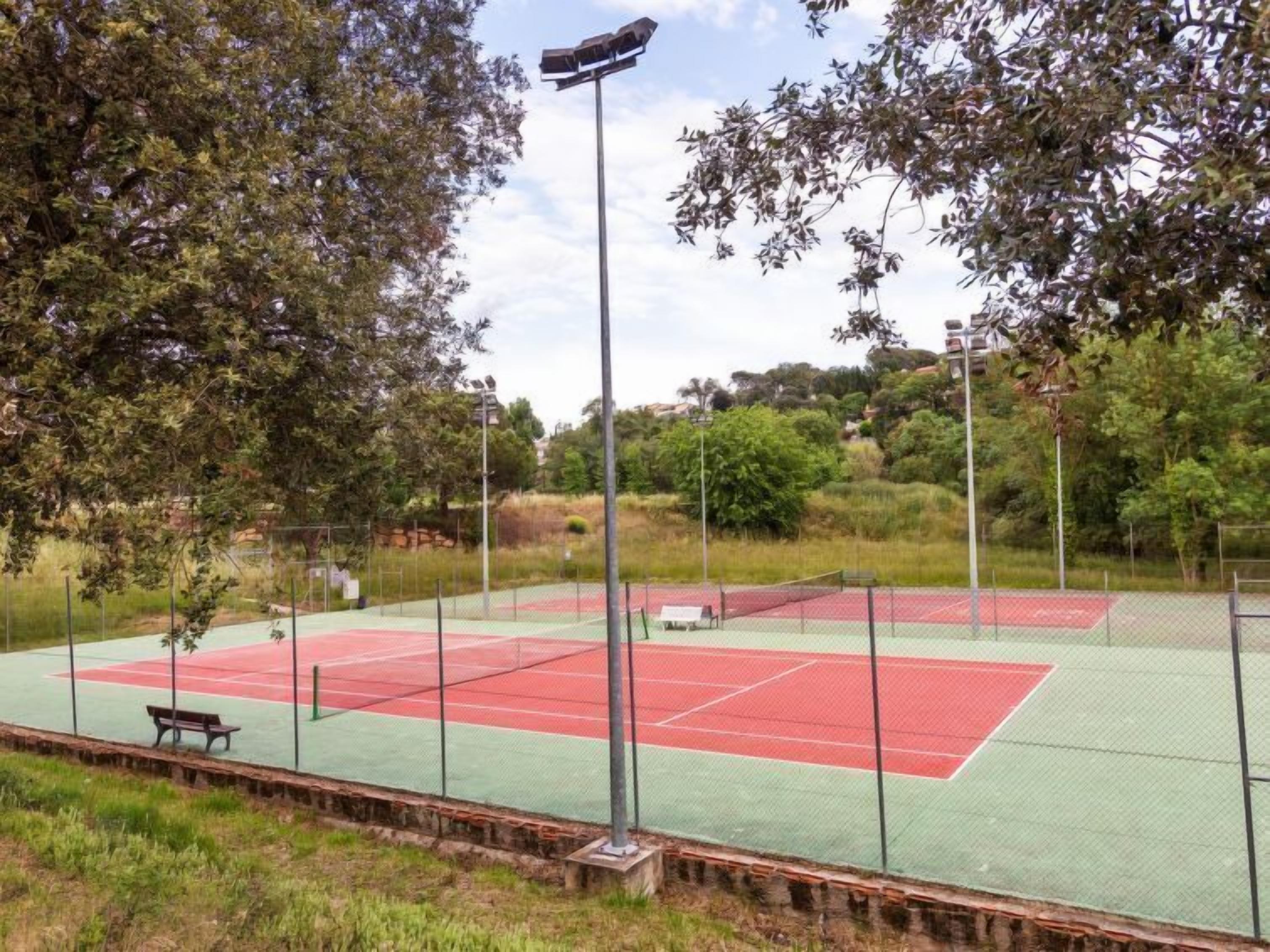 An outdoor tennis court with a fence, benches, and trees in the background.