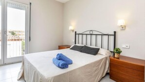 Un lit bien fait, recouvert d’une courtepointe blanche et agrémenté de deux oreillers, une table de chevet en bois avec une lampe, et une petite plante posée sur la table de chevet.