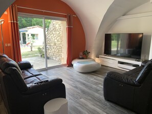 A modern living room with a large TV, leather sofas, a stone wall, and a sliding glass door leading to an outdoor area. - Domaine de la Bergerie en Drôme Provençale (SAUZET)