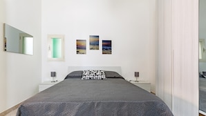 Ein Schlafzimmer mit einem großen Bett, zwei Nachttischen, einem Beistelltisch und drei an der Wand hängenden Landschaftsbildern.