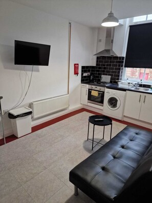 Compact kitchenette with stove, oven, microwave, and flat-screen TV, offering a functional space for cooking and relaxation.