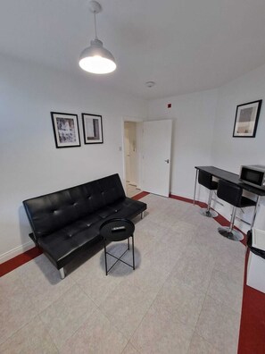 Cozy living space with a sofa, table, and chair, featuring a door to another room.