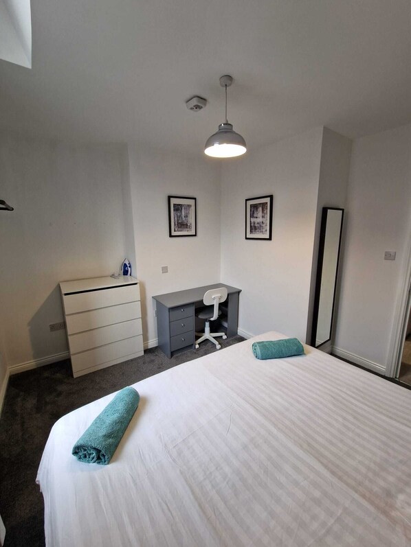 Comfortable retreat with a large bed, dresser, desk, and framed artwork.