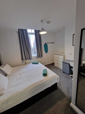 Relax in a serene bedroom with a large bed, desk, and black-framed mirror.