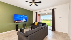 Een woonkamer met een flatscreen televisie, een bank, een glazen salontafel en een plafondventilator.