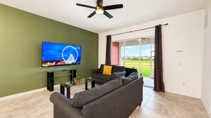 Un salon équipé d’un téléviseur à écran plat, d’un canapé, d’une table basse en verre et d’un ventilateur de plafond.