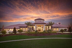 A large, single-story house with a central circular structure, surrounded by a well-maintained lawn and palm trees.