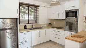 Une cuisine moderne avec des meubles blancs, des appareils en acier inoxydable, une fenêtre avec des stores et un plan de travail en bois.