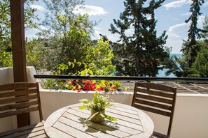 A round table with a wicker centerpiece, two wooden chairs, and a view of a garden with various plants and flowers. - Grand Bleu Porto Heli Beachfront House (Ermionida)