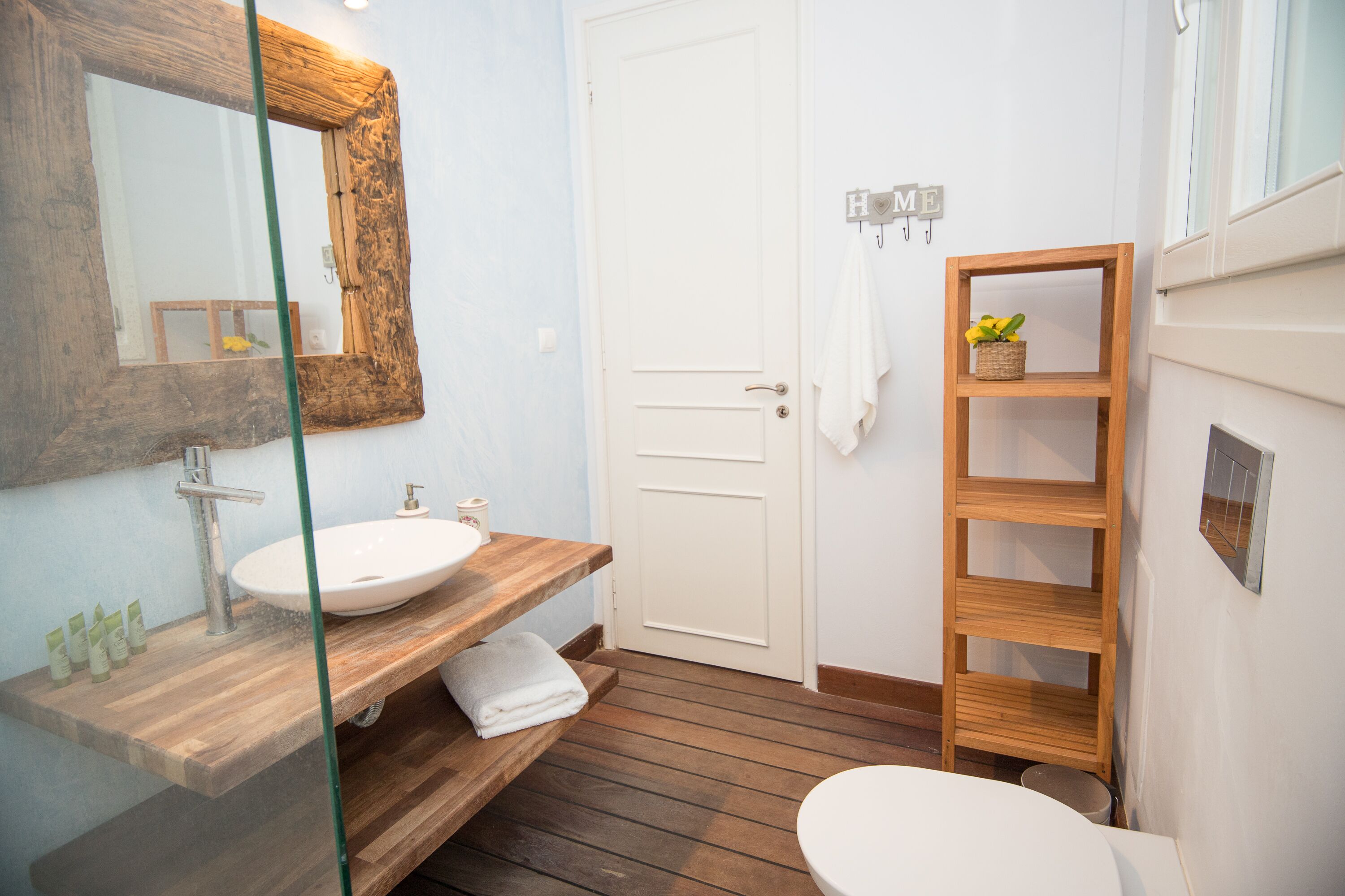 A bathroom with a wooden vanity, a white sink, a large mirror, a white toilet, and a wooden shelf with a plant.