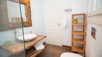 Un baño con tocador de madera, un lavamanos blanco, un espejo grande, un inodoro blanco y una repisa de madera con una planta.