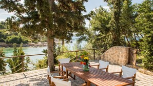 Une terrasse en bois avec une table et des chaises, donnant sur une étendue d’eau et entourée d’arbres.