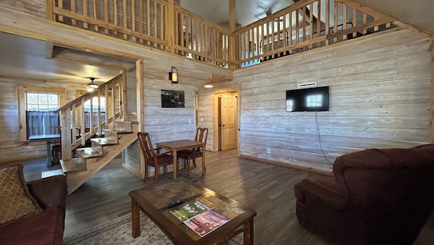 A spacious living area with a wooden staircase, a dining table with chairs, a sofa, and a television mounted on the wall. - Park and ride to the ATV trailhead and the Mulberry River at Cass Arkansas. (Ozark)