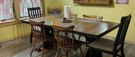 A dining table with four wooden chairs, a roll of paper towels, and a small basket on the table.