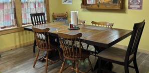 Uma mesa de jantar com quatro cadeiras de madeira, um rolo de papel toalha e uma pequena cesta sobre a mesa.
