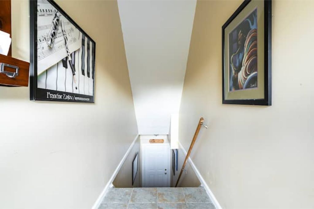 Un couloir étroit, avec une porte au fond, et de chaque côté, deux tableaux encadrés.