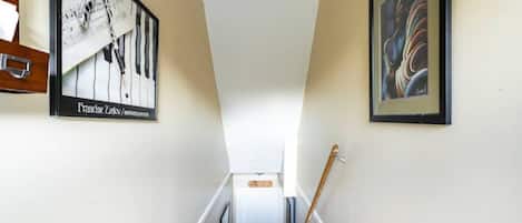Un couloir étroit, avec une porte au fond, et de chaque côté, deux tableaux encadrés.