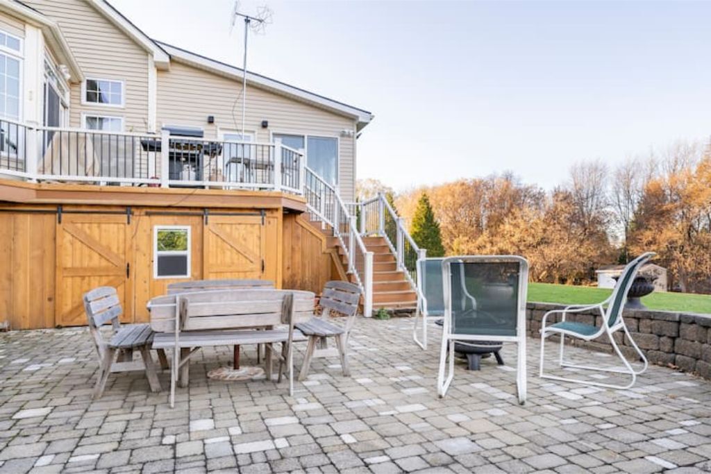 Un patio con terraza de madera, mobiliario exterior y vista a una casa con balcón.