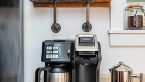 A coffee maker with a control panel, a stainless steel pot, and a wooden shelf with white mugs. - Artisan Gem - 2 BR / 1 Bath (Spruce Pine)