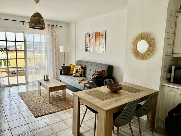 Un salon moderne avec un canapé, une table à manger et des chaises. Il y a une grande fenêtre avec des rideaux, une lampe et des œuvres d’art accrochées au mur.