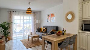 Ein modernes Wohnzimmer mit einer Couch, einem Esstisch mit Stühlen, einem Fernseher und einer Küchenzeile mit Schränken.