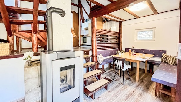 A rustic kitchen with a wood stove, wooden beams, a dining area with benches, and a window with a view. - Rumpelstilzchen by Interhome (Frankenau)