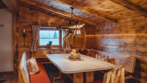 Interior de una cabaña de madera con una mesa de comedor, bancos y una ventana con vistas.